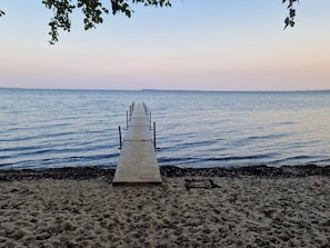 Une jetée en bois s’étendant dans une eau calme, entourée d’une plage de sable.