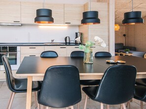 Cozinha moderna com armários de madeira, bancada preta e área de refeições com mesa de madeira e cadeiras pretas.
