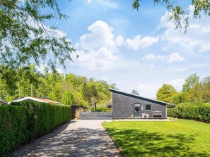 A modern house with a gravel driveway, surrounded by lush greenery and trees.