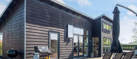 A modern house with a deck, a barbecue, and outdoor seating.