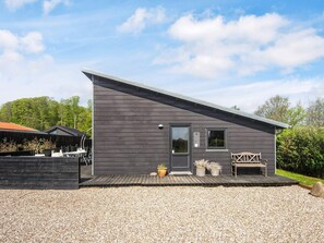A modern building with a dark exterior, a front door, a small window, and a wooden deck with outdoor seating.