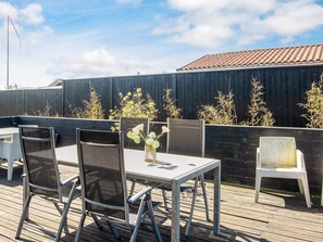 An outdoor patio with a table and chairs, a wooden deck, and a dark fence. - 4 Star Holiday Home in Bjert (Bjert)