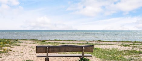 A bench on a sandy beach with a view of the sea and sky.