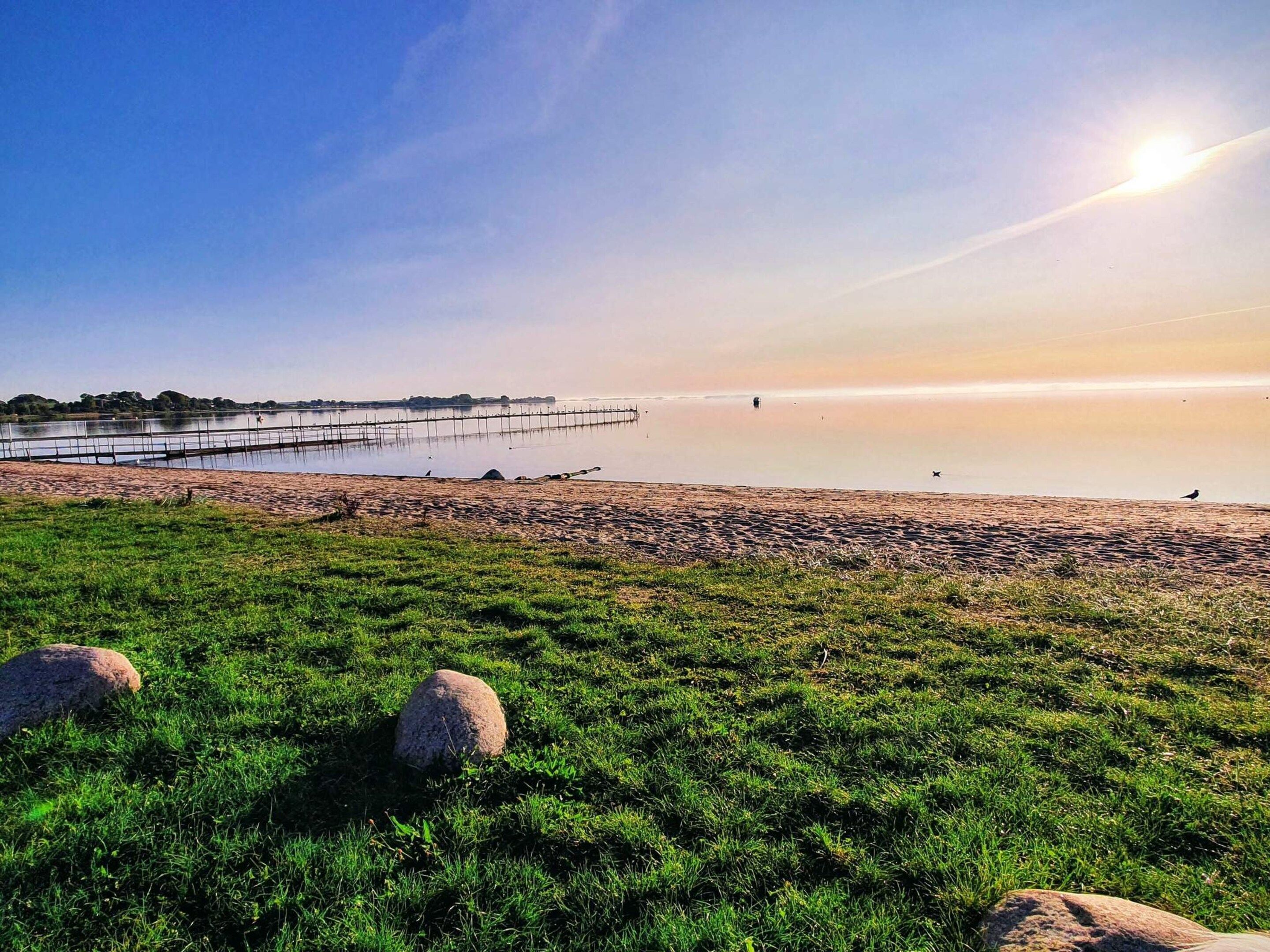 A beach with a clear sky, calm water, and a distant shoreline.
