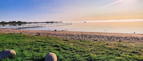 A beach with a clear sky, calm water, and a distant shoreline.