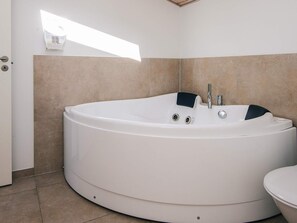 A modern bathroom with a large freestanding bathtub, a toilet, and a small window providing natural light. - 4 Star Holiday Home in Bjert (Bjert)