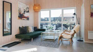 A spacious living room with a green sofa, a coffee table, and a wicker chair. Large windows provide a view of the backyard. - 4 Star Holiday Home in Bjert (Bjert)