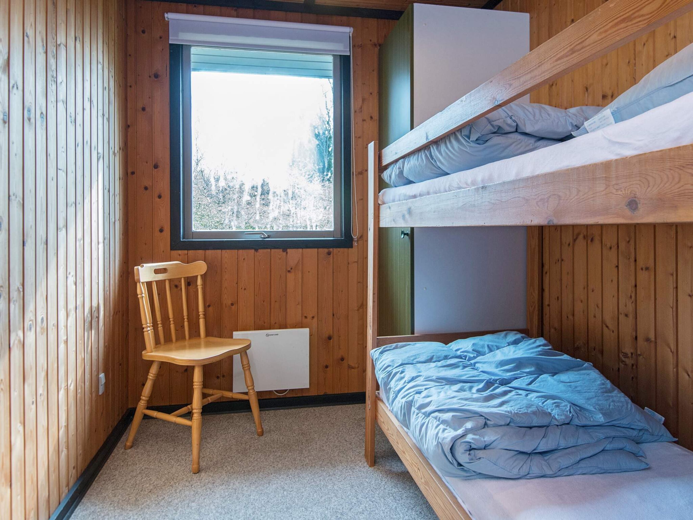 A bunk bed room with a window, a wooden chair, and a desk.