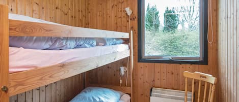 Una habitación con literas, una silla y una ventana con vistas a árboles.