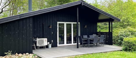 A black wooden cabin with a covered patio, a sliding glass door, and outdoor furniture.