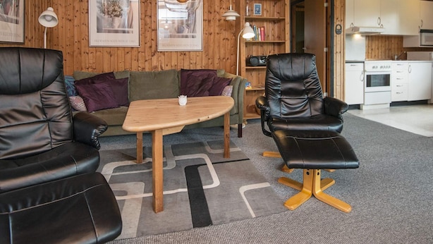 A cozy room with a wooden ceiling, a sofa, a chair, a small table, and a kitchen area in the background. - 6 Person Holiday Home in Toftlund (Toftlund)