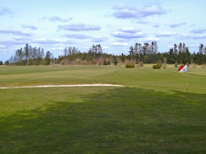 Un parcours de golf avec un bunker de sable et un drapeau indiquant le trou.