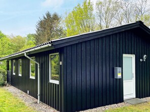 Un bâtiment en métal noir doté d’une porte, de fenêtres et d’un petit espace extérieur recouvert de gravier.