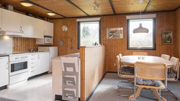 A modern kitchen with white cabinets, a microwave, and a stove. There is a dining area with a round table and wicker chairs.