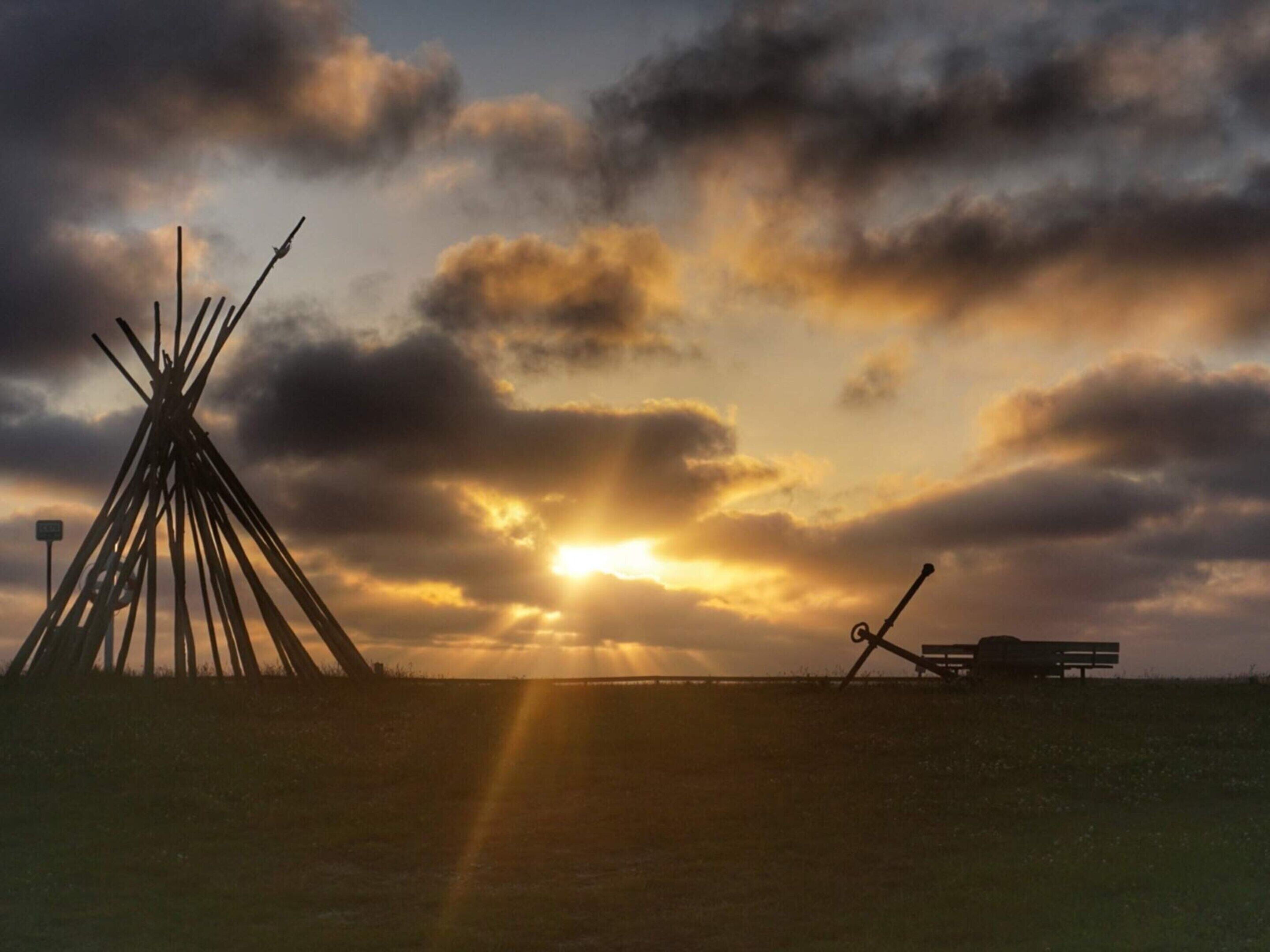 En tipi och en bänk på en gräsklädd äng med en solnedgång i bakgrunden.