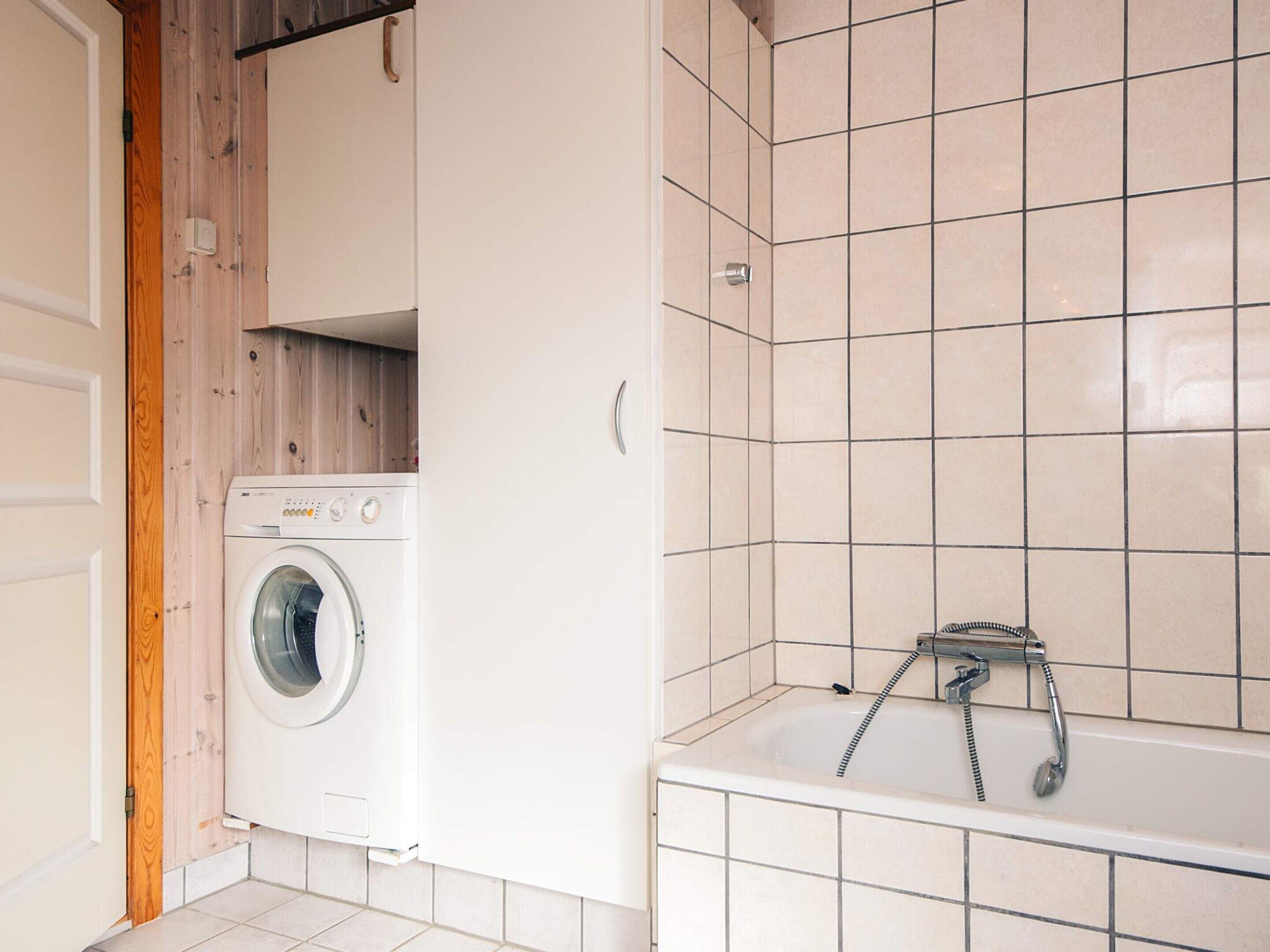 A laundry room with a washing machine, a shower with a hose, and tiled walls.