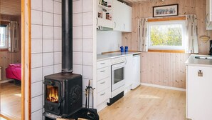 A cozy cabin-style kitchen with a wood-burning stove, white cabinetry, and a window with a view of greenery. - 6 Person Holiday Home in Tarm-by Traum (Tarm)