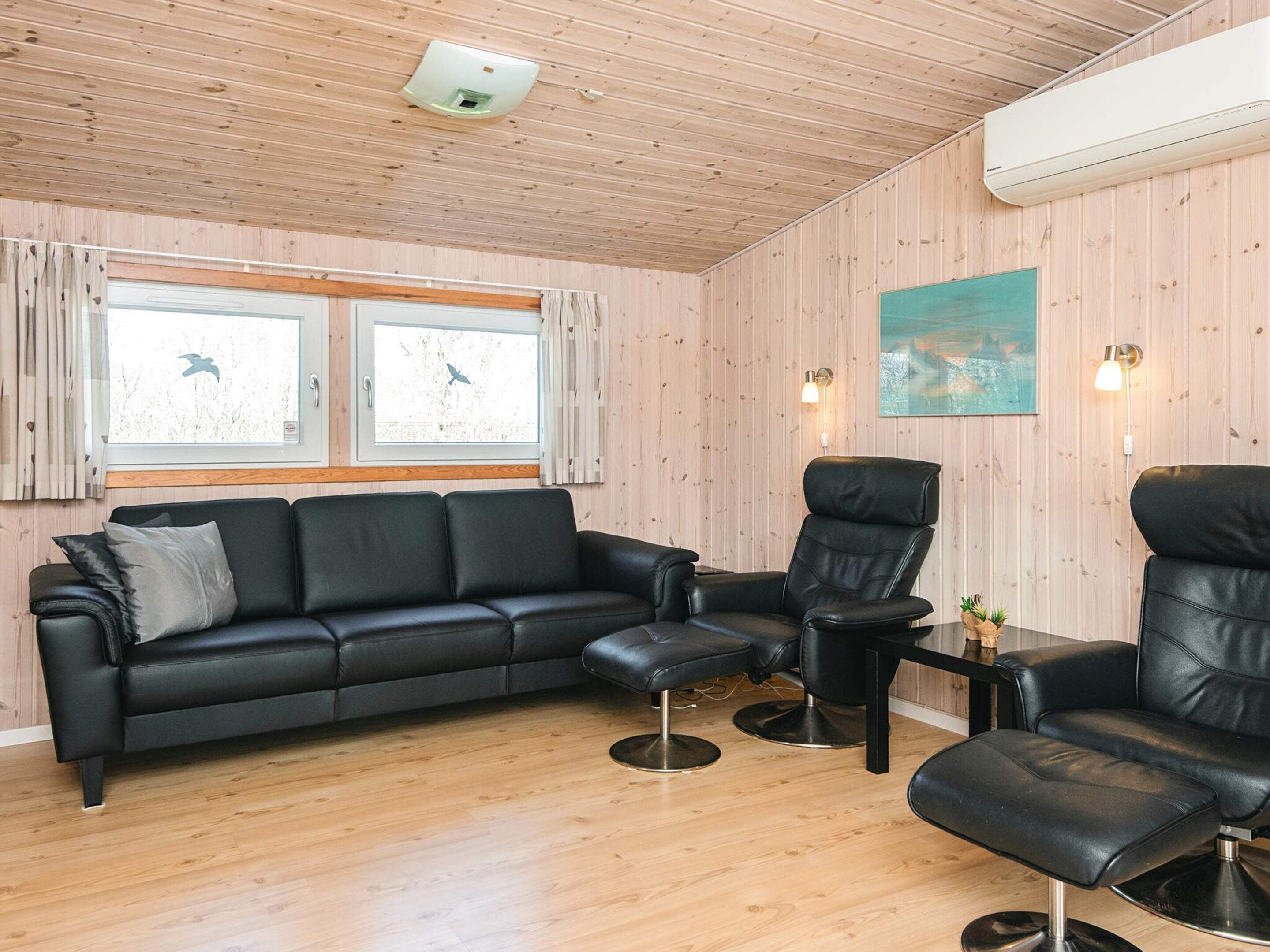 Ein modernes Wohnzimmer mit einem schwarzen Ledersofa, zwei schwarzen Ledersesseln, einem kleinen Tisch und einem Fenster mit Vorhängen.