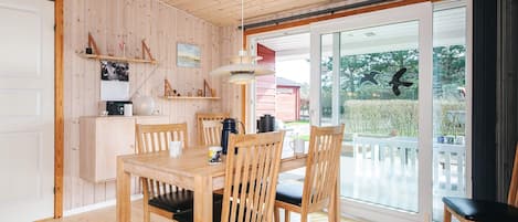 A wooden-paneled room with a dining table and chairs, a coffee maker, and a view of the outdoors through a glass door.