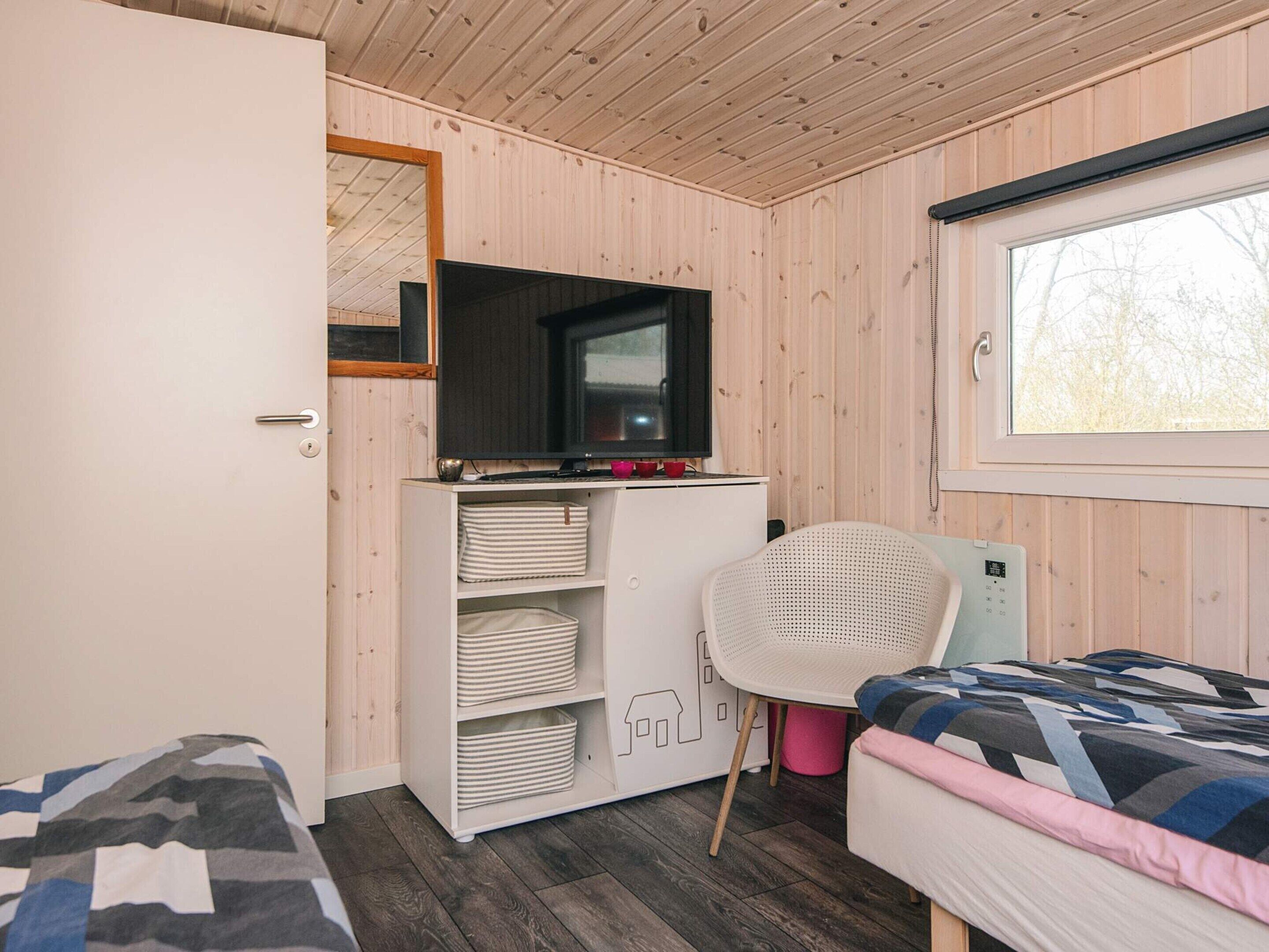 A bedroom with a bed, a desk with storage, a chair, a television, and a window.