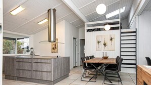 A modern kitchen with a central island, a dining area with a wooden table and chairs, and a staircase leading to an upper level. - 5 Star Holiday Home in Knebel (Knebel)