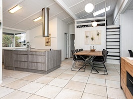 A modern kitchen with a central island, a dining area with a wooden table and chairs, and a staircase leading to an upper level.