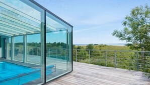 A modern glass-enclosed infinity pool with a wooden deck and a metal railing. - 5 Star Holiday Home in Knebel (Knebel)