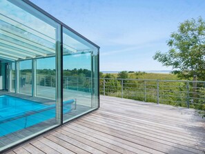 A modern glass-enclosed infinity pool with a wooden deck and a metal railing. - 5 Star Holiday Home in Knebel (Knebel)