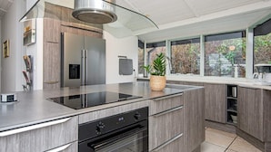 A modern kitchen with a stainless steel range hood, built-in oven, and a large window offering a view of the outdoors. - 5 Star Holiday Home in Knebel (Knebel)