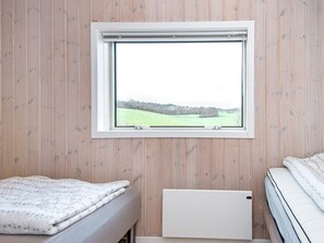 A room with a bed, a window with a view of a field, and wooden paneling on the walls.