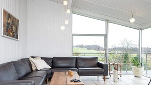 A modern living room with a black leather sectional sofa, a wooden coffee table, and a large window offering a view of a green landscape. - 5 Star Holiday Home in Knebel (Knebel)