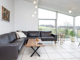 A modern living room with a black leather sectional sofa, a wooden coffee table, and a large window offering a view of a green landscape.
