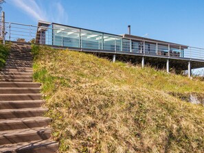 A modern building with a glass facade, a metal staircase leading up to it, and a grassy hill in the foreground.