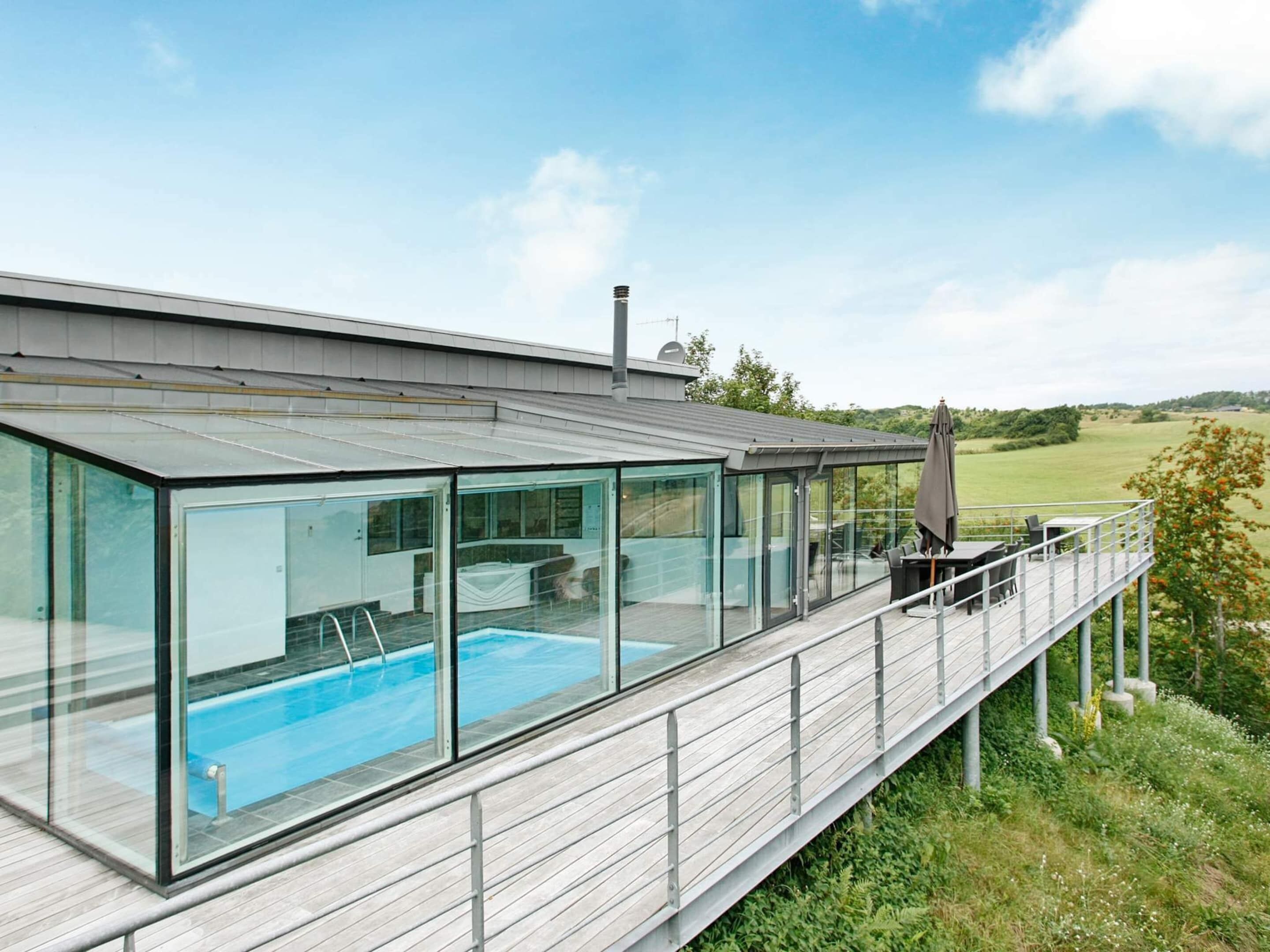 A modern house with a glass-enclosed swimming pool, a deck with outdoor furniture, and a view of the countryside.