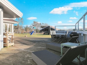 A wooden deck with outdoor furniture, a barbecue grill, and a playground in the background.