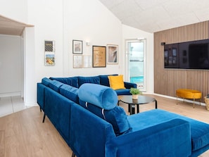 A modern living room with a blue sectional sofa, a small round table, and a flat-screen TV mounted on the wall. - 5 Star Holiday Home in Harboore (Harboore)