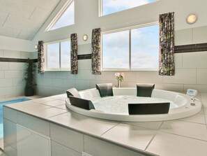 A modern bathroom with a freestanding bathtub, a window with patterned curtains, and a potted plant.