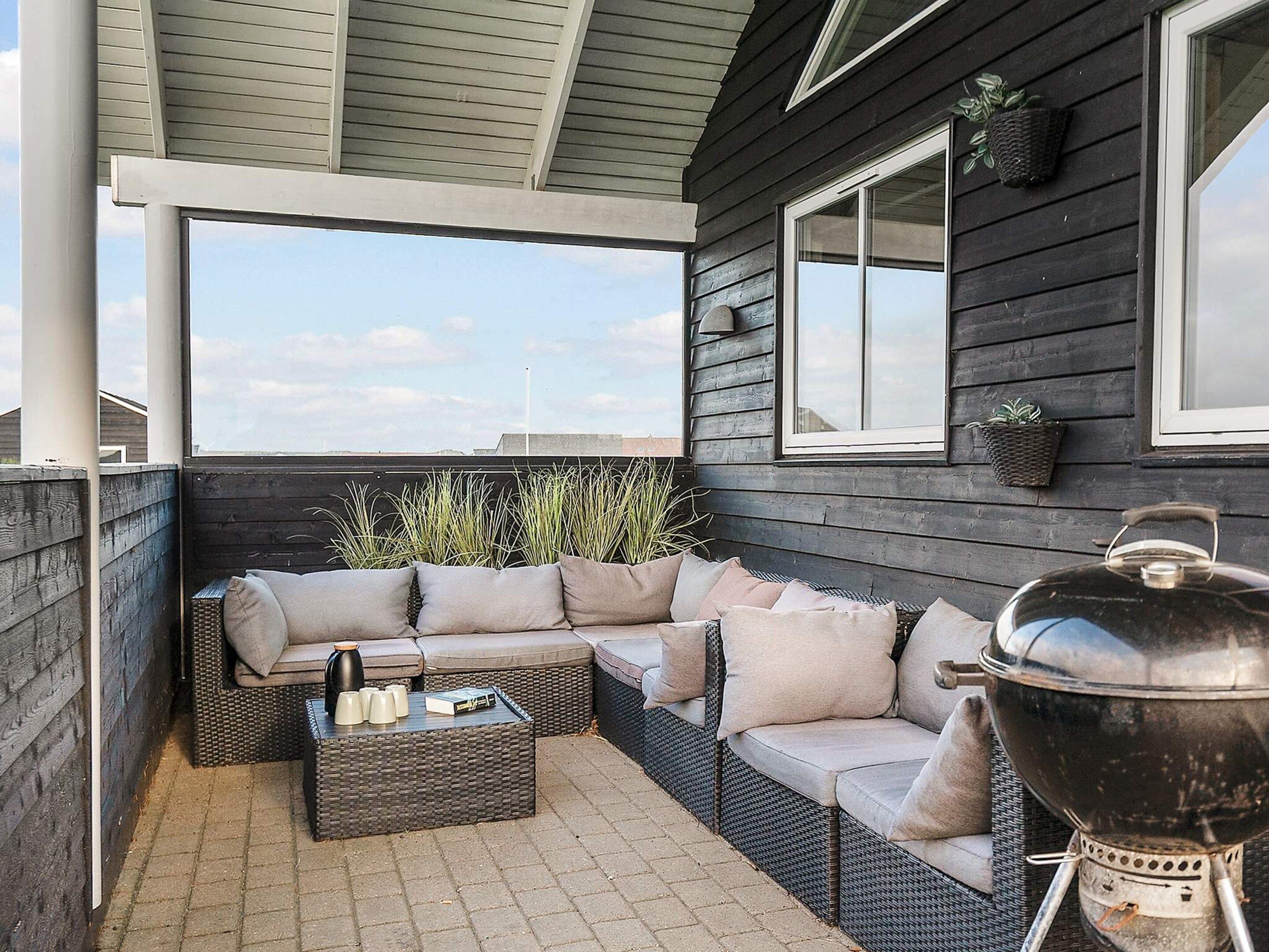 A covered outdoor seating area with a sofa and a coffee table, a grill, and potted plants.