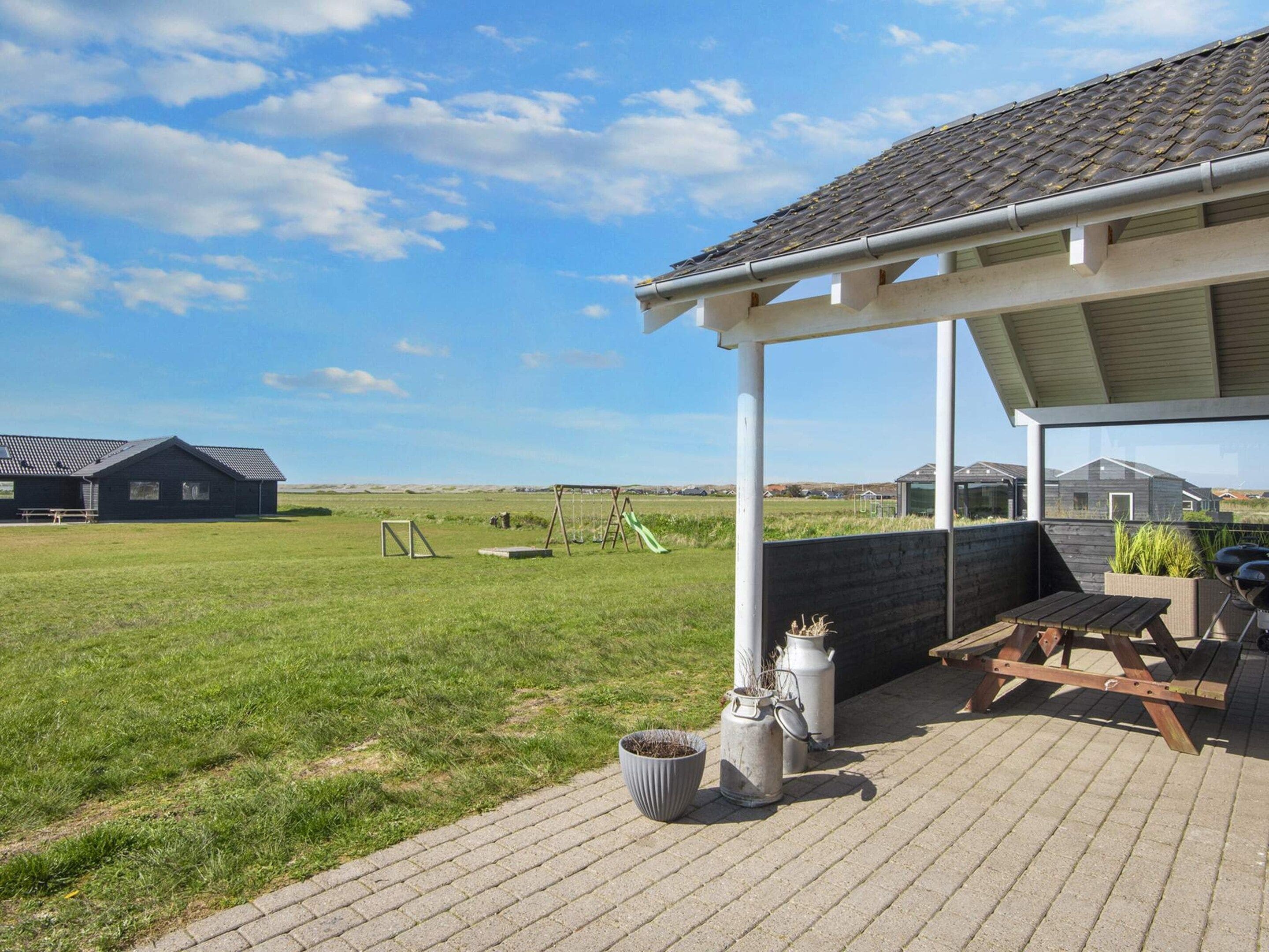 Un patio couvert avec vue sur un champ verdoyant et une maison en arrière-plan.
