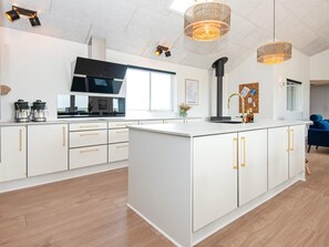 Cozinha moderna com armários brancos, uma ilha central e luminárias pendentes.