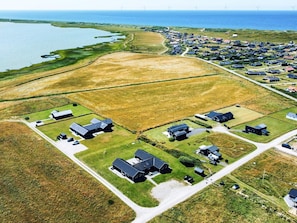 An aerial view of a coastal residential area with houses, wind turbines, and a body of water. - 5 Star Holiday Home in Harboore (Harboore)