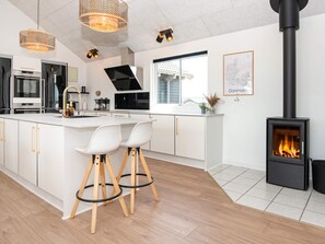 A modern kitchen with a central island, bar stools, a stove, and a large window. - 5 Star Holiday Home in Harboore (Harboore)