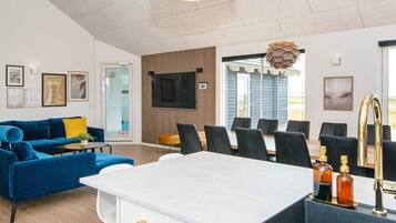 En moderne stue med en blå sofa, et hvidt spisebord og et køkkenområde med vask og barstole.
