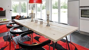 Une cuisine moderne avec une longue table en bois, des tabourets de bar noirs, un luminaire suspendu rouge et un micro-ondes encastré.