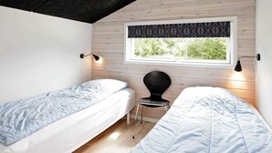 Une chambre avec deux lits, une fenêtre avec un store à motifs et deux lampes fixées au mur.