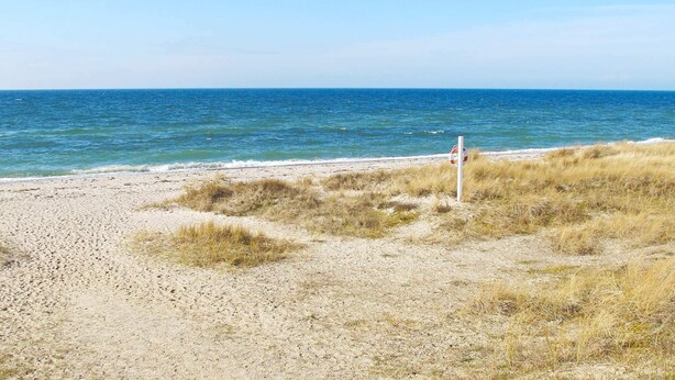 Ein Strand mit Rettungsschwimmer-Schild, Sandufer und dem Meer.