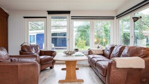 Ein geräumiges Wohnzimmer mit Ledersofas, einem Holztisch und großen Fenstern mit Blick ins Freie.