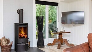 Ein gemütliches Wohnzimmer mit Kaminofen, Fernseher und Ledersofa.
