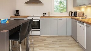 Eine kleine Küche mit Herd, Mikrowelle und Spüle, Holz Arbeitsplatten und einem Fenster mit Blick auf Bäume.