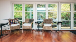 Una habitación con tres sillas de mimbre, piso de madera y ventanas amplias que dan a vistas de vegetación.